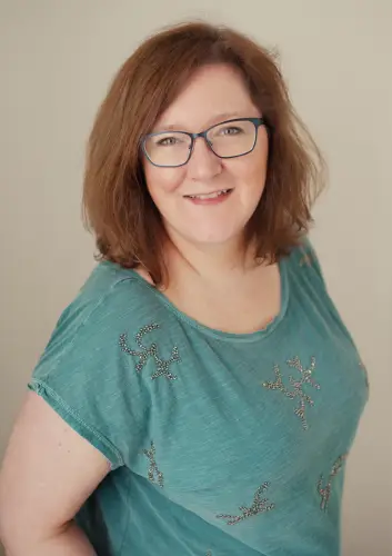 White woman (Rebecca Scott-Pillai) smiling at the camera. She wears a green top.